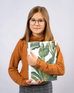 Portret szkolny dziewczynki w okularach i w beżowym swetrze trzymającej książkę w kwiecistej okładce