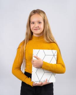 Portret szkolny dziewczynki w żółtym swetrze z książką w ręce