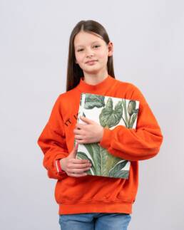 Portret szkolny dziewczynki w pomarańczowej bluzie z książką w ręce